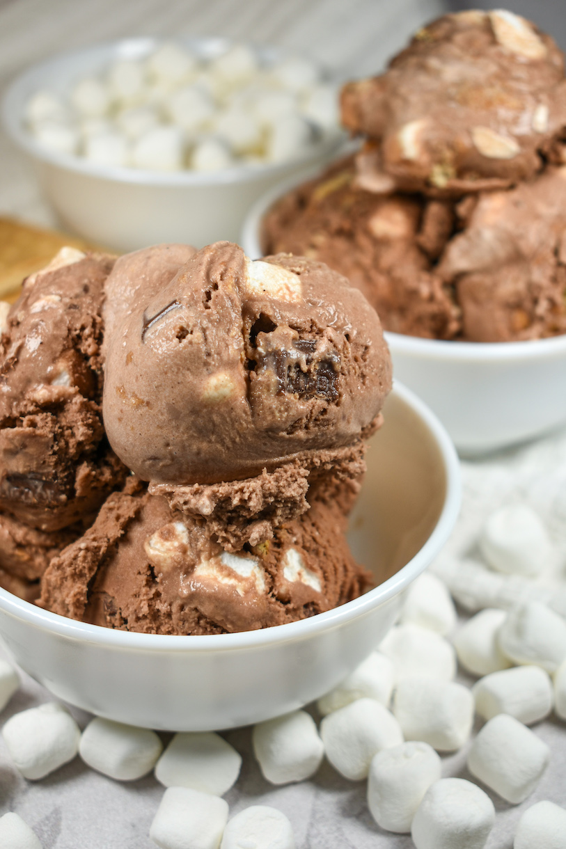 Two bowls of smores ice cream and a dish of mini marshmallows on a white surface