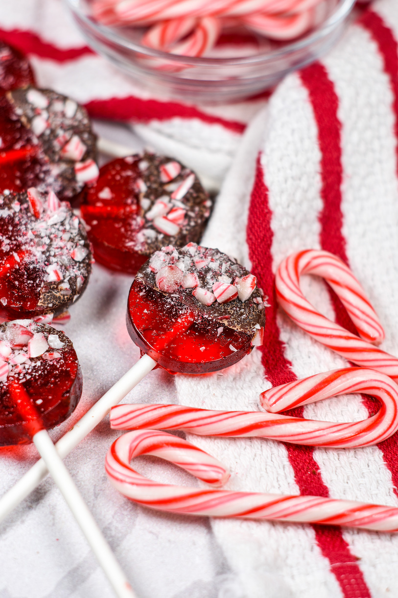 Red peppermint lollipops dunked in dark chocolate, surrounded by a striped towel and miniature candy canes