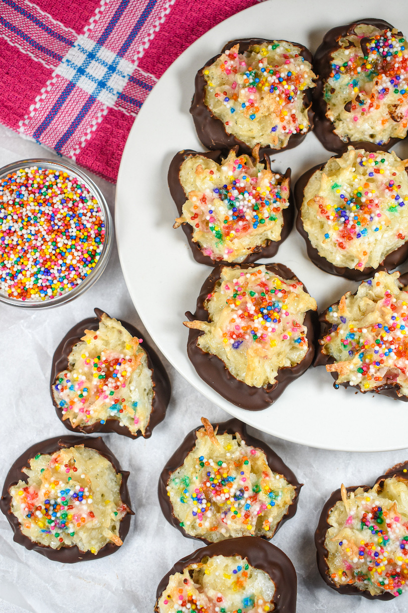 A plate of chocolate dipped birthday cake coconut macaroons and a dish of sprinkles