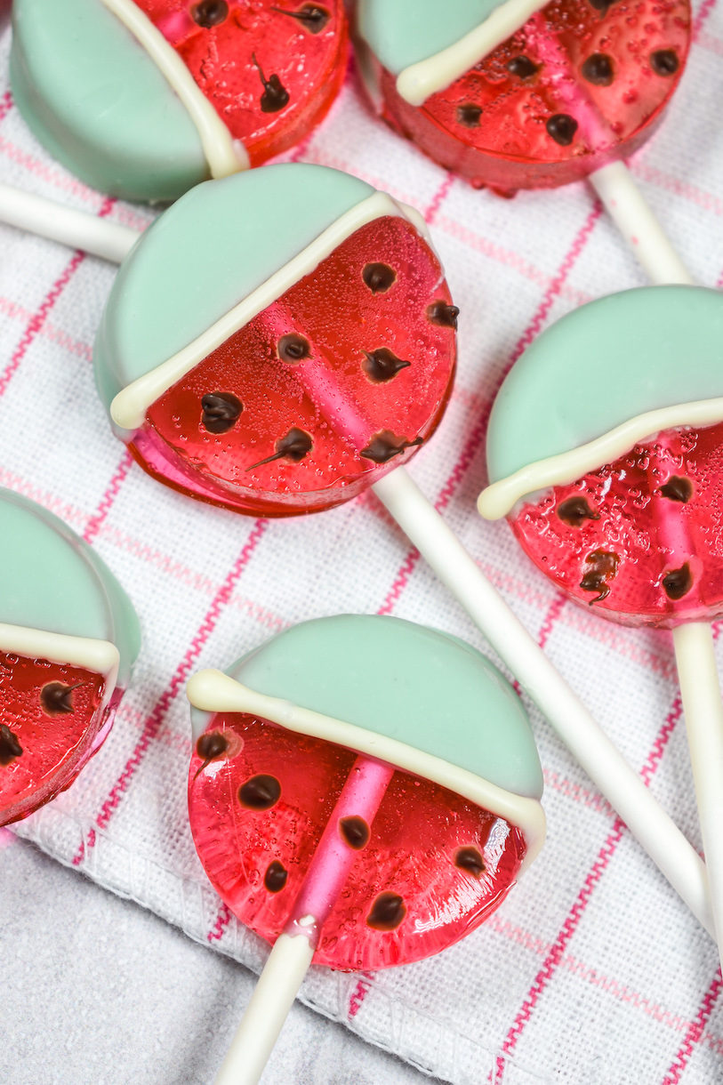 Pink and green watermelon lollipops arranged on a plaid towel