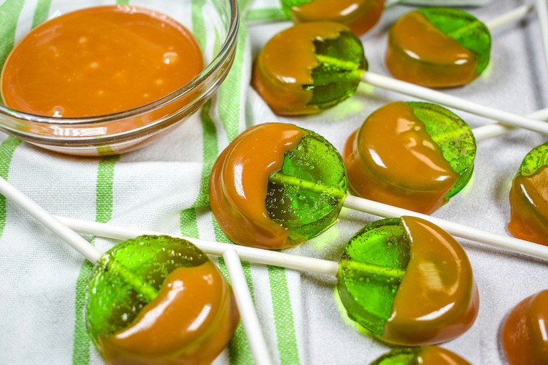 Caramel apple lollipops on a white surface