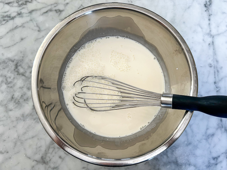 Milk, cream, and whisk in a metal bowl