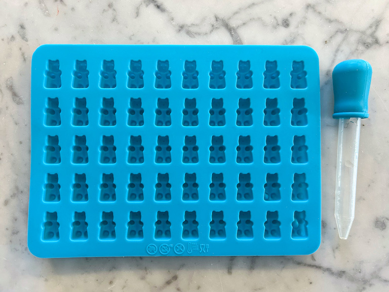 Blue silicone gummy bear mold and an eye dropper, used for making homemade gummy bears