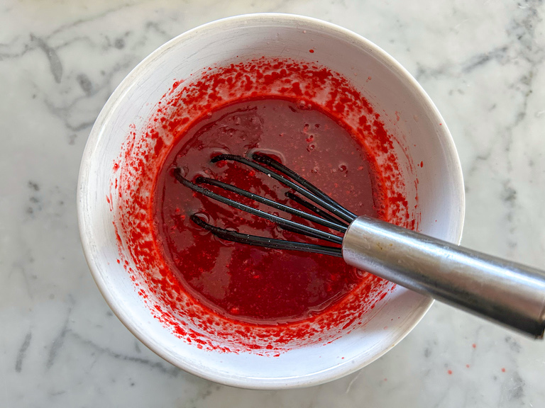 Red jello mixture and whisk in a bowl