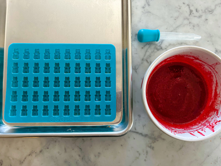 Metal tray, gummy bear mold, eye dropper, and bowl of red gelatin