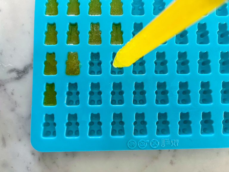 Eyedropper dropping yellow gummy bear mixture into silicone mold