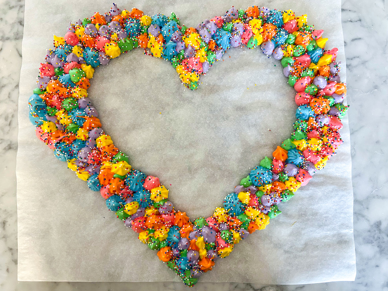 A piped rainbow meringue wreath on a sheet of parchment