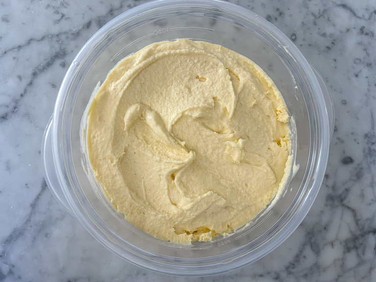 soft mango ice cream in a plastic container on a marble countertop