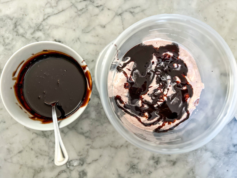 Dish of fudge sauce and container of strawberry ice cream with pools of fudge sauce