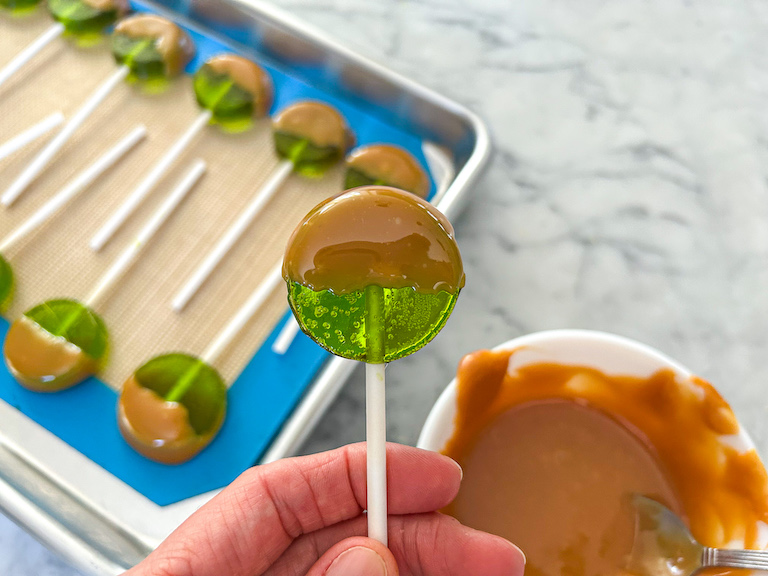 Hand holding an apple lollipop dipped in melted caramel