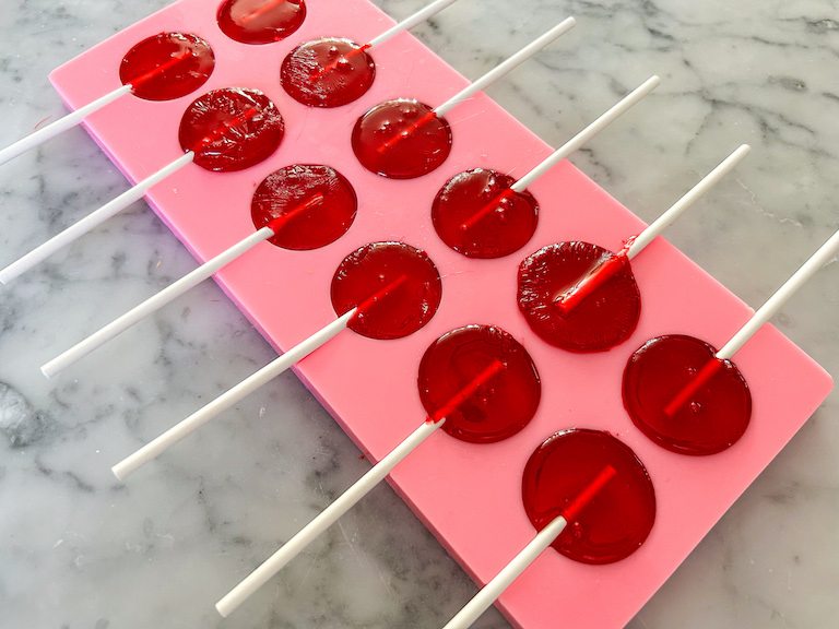 Silicone lollipop mold filled with red sugar syrup