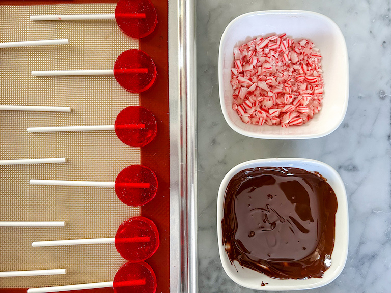 Dish of melted chocolate, dish of peppermint, and red lollipops on a tray