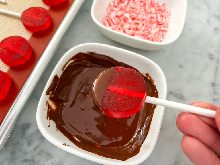 Dipping a peppermint lollipop in melted chocolate