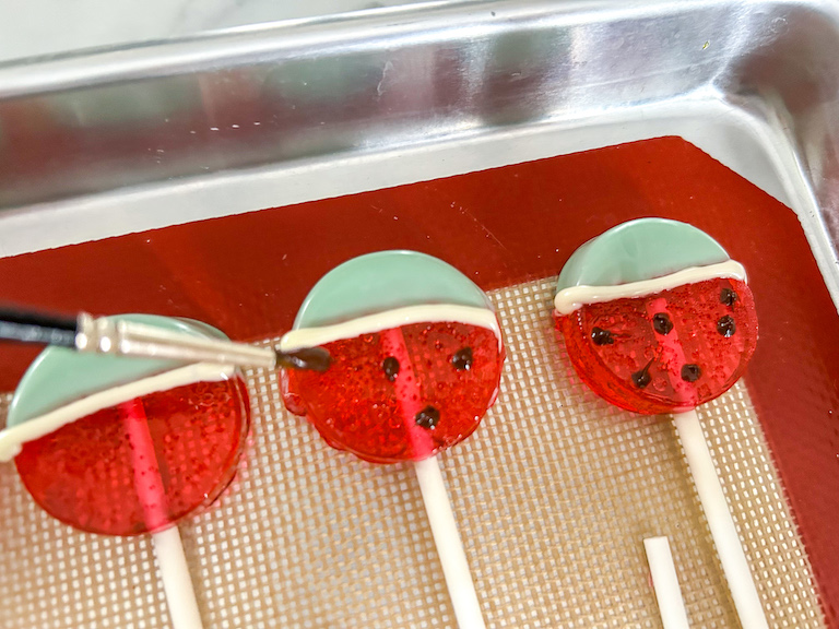 Paintbrush applying chocolate dots to watermelon lollipop