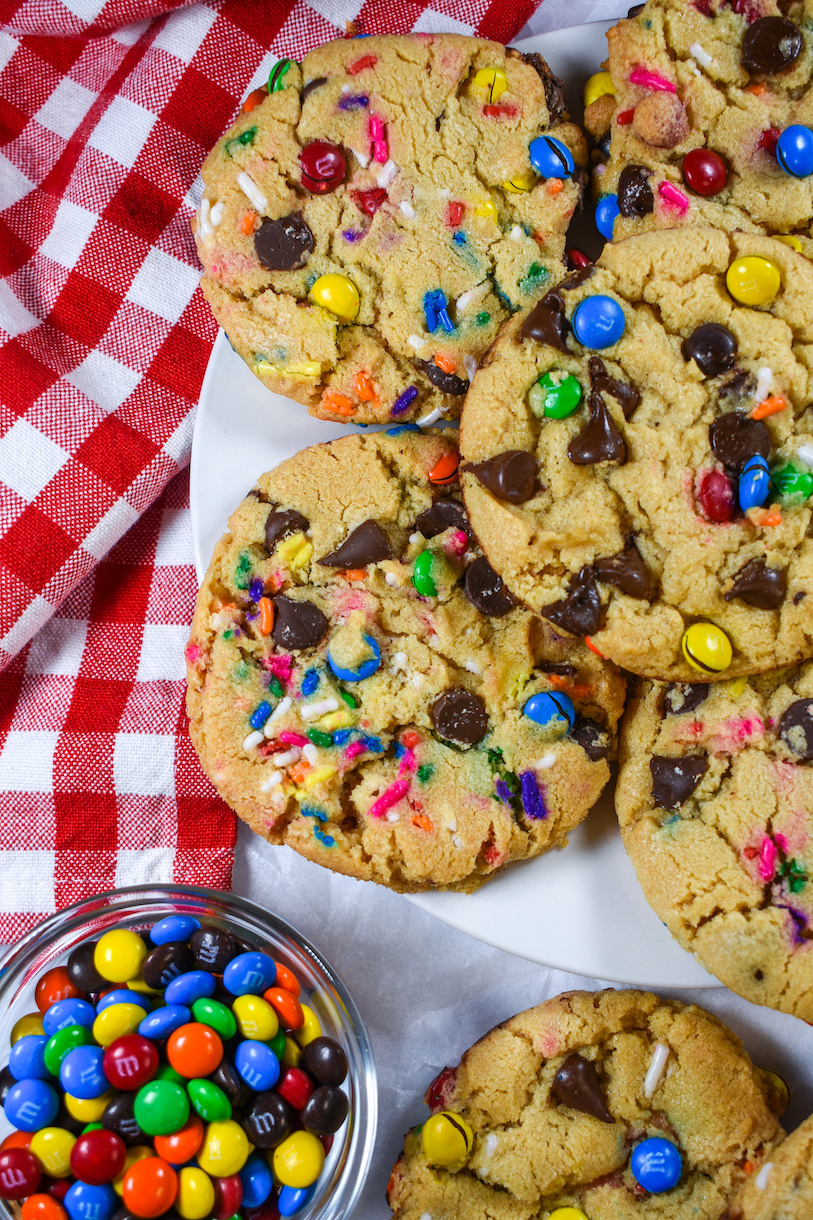 Rainbow cookies on a plate next to a bowl of M&Ms and a red checkered towel