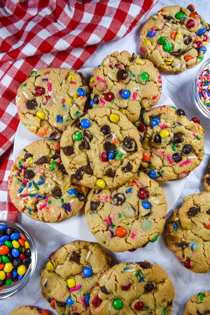 Rainbow M&M cookies on a white surface with a red checkered tea towel