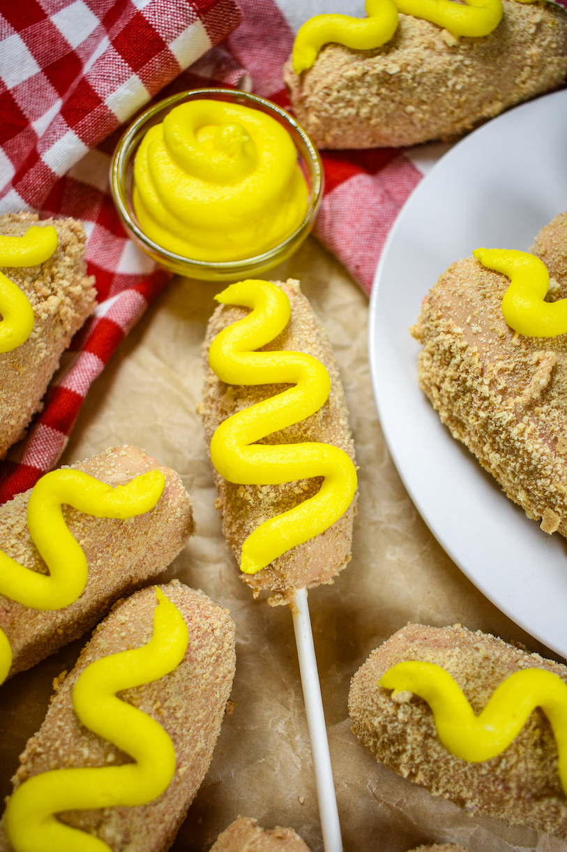 Corn dog cake pops and a dish of buttercream mustard on a sheet of parchment