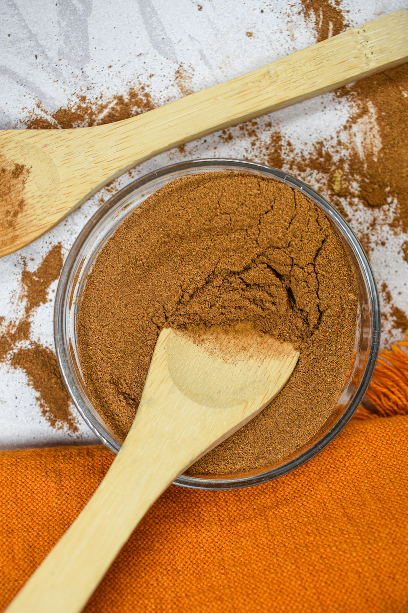 Dish of pumpkin spice mix with two wooden spoons and an orange towel