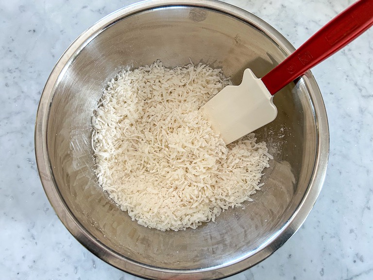 Coconut, sugar, and flour in a bowl with a rubber spatula