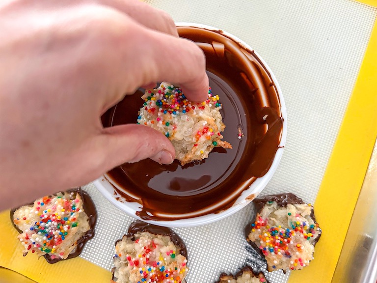 Hand dipping a macaroon in melted chocolate