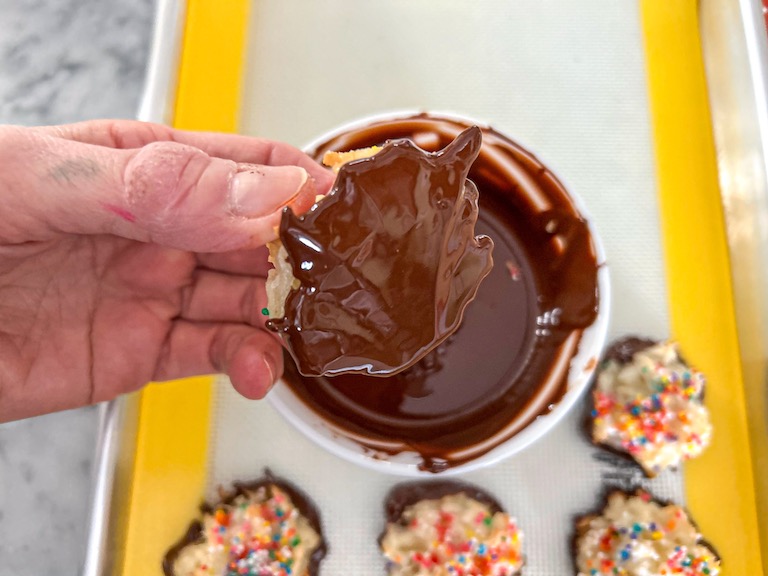 Hand dipping a coconut macaroon in chocolate