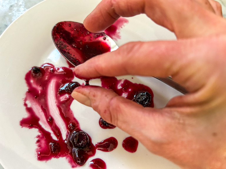 Fingers checking homemade jam for thread stage