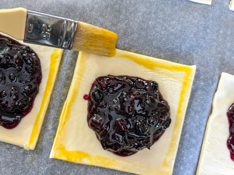 egg washing edges of a mixed berry hand pie