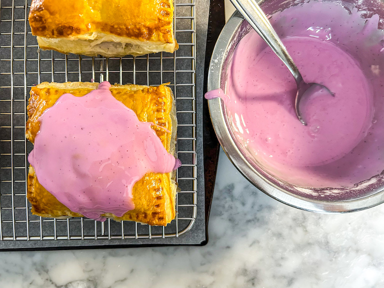 Mixed berry hand pies on a rack with a dish of purple glaze