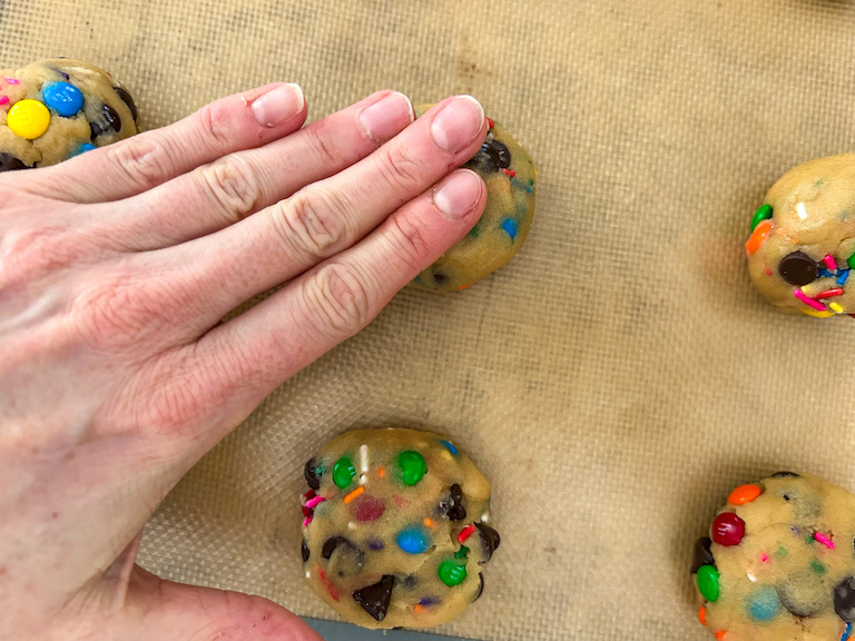 Hand pressing down balls of cookie dough