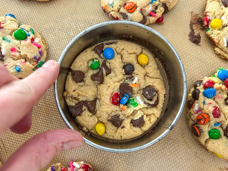 Hand reshaping a cookie with a round cutter