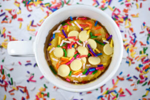 A funfetti mug cake surrounded by rainbow sprinkles