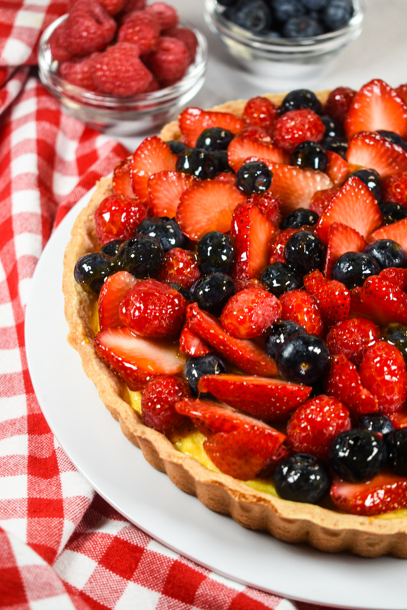 a berry fruit tart on a white plate with a checkered tea towel