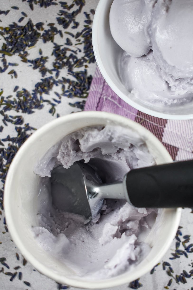 A cardboard container of lavender ice cream and a metal ice cream scoop