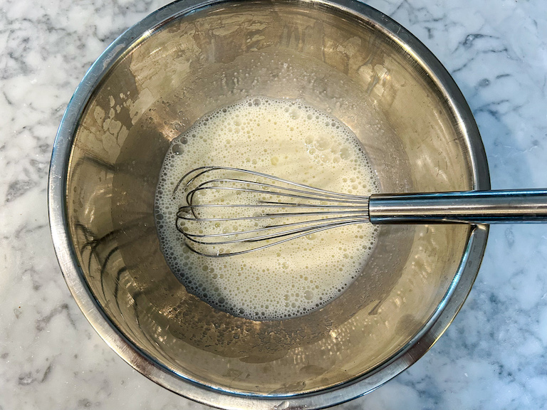 Frothy egg white mixture in bowl with whisk