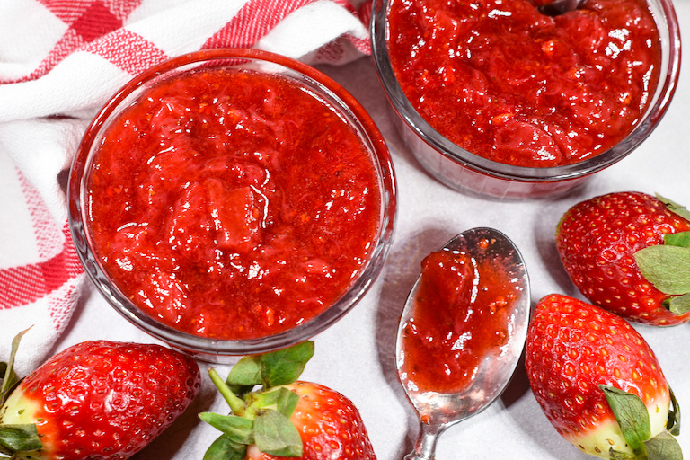 Dishes of bright red strawberry fruit compote, fresh berries, and a spoon