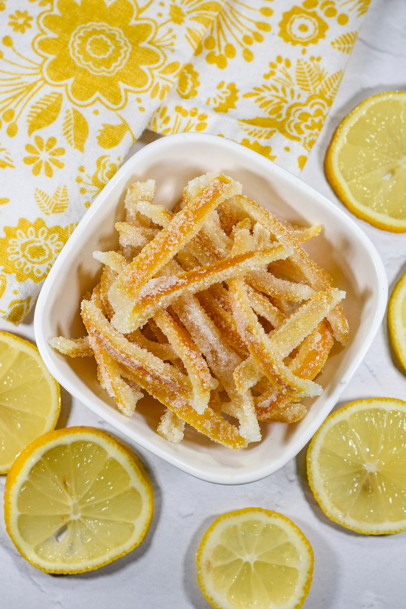 A dish of candied lemon peels surrounded by fresh lemon slices