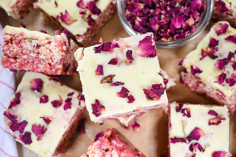 A stack of pink krispie treats with white chocolate and rose petals on top