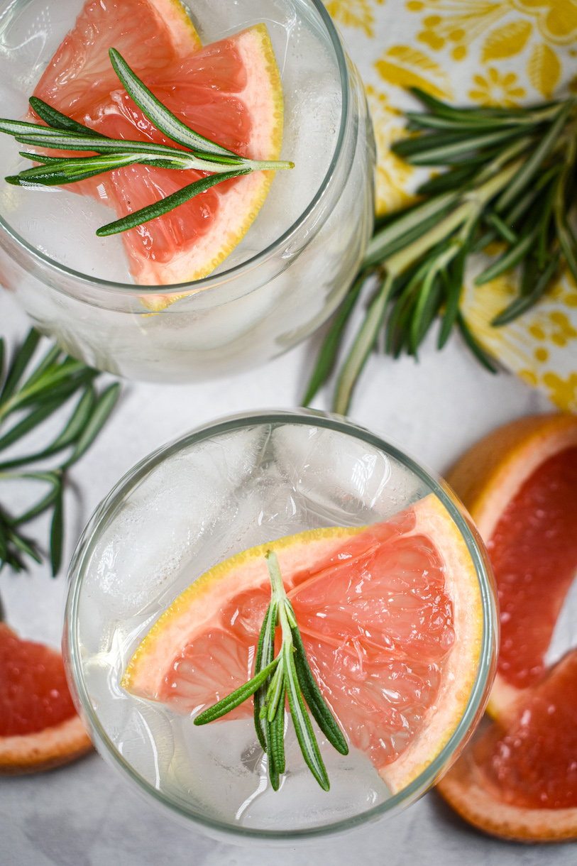 Looking down at glasses of grapefruit water garnished with sprigs of rosemary and grapefruit slices