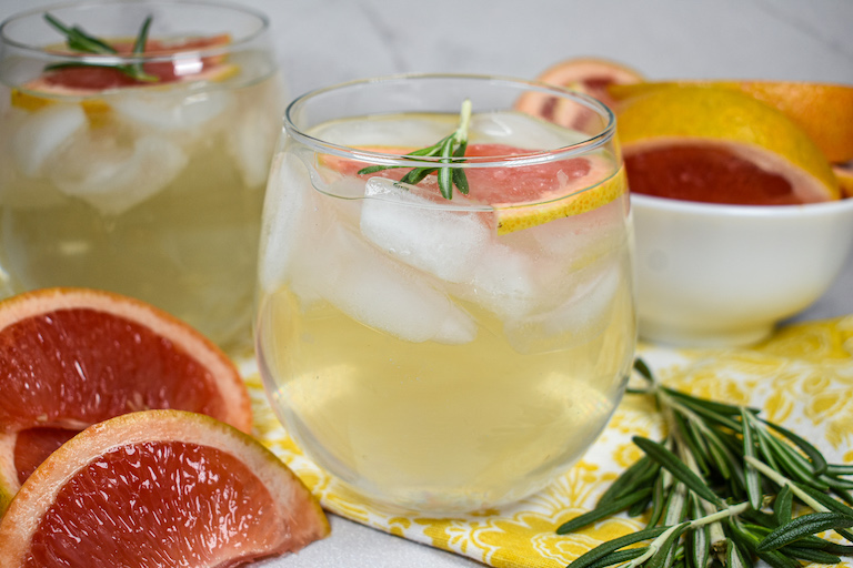 Glasses of grapefruit water surrounded by slices of grapefruit and sprigs of rosemary