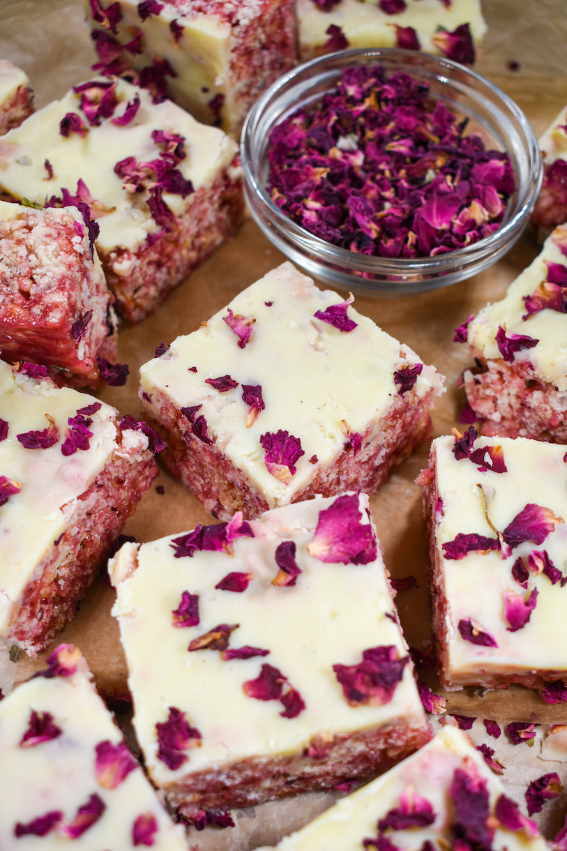 Pink krispie treats topped with white chocolate ganache, and a bowl of rose petals