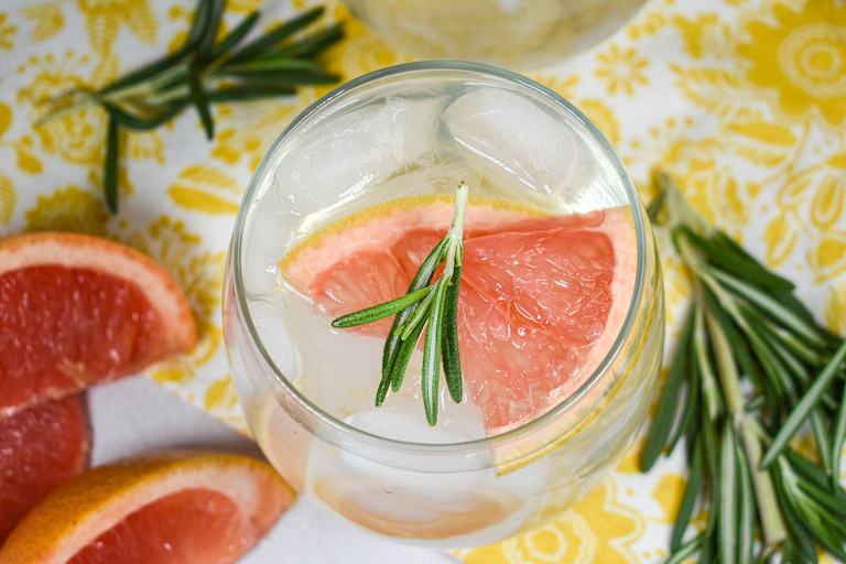 A glass of grapefruit water garnished with grapefruit and rosemary