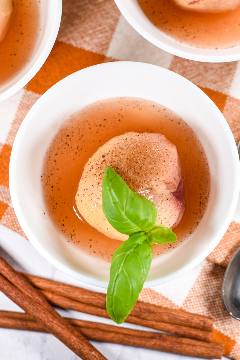 A poached peach in a bowl with basil garnish