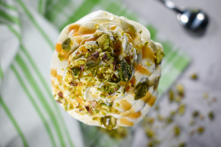 Looking down at a milkshake garnished with whipped cream, pistachios, and caramel sauce