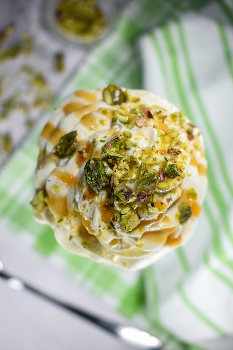looking down at a milkshake with whipped cream, pistachios and caramel sauce