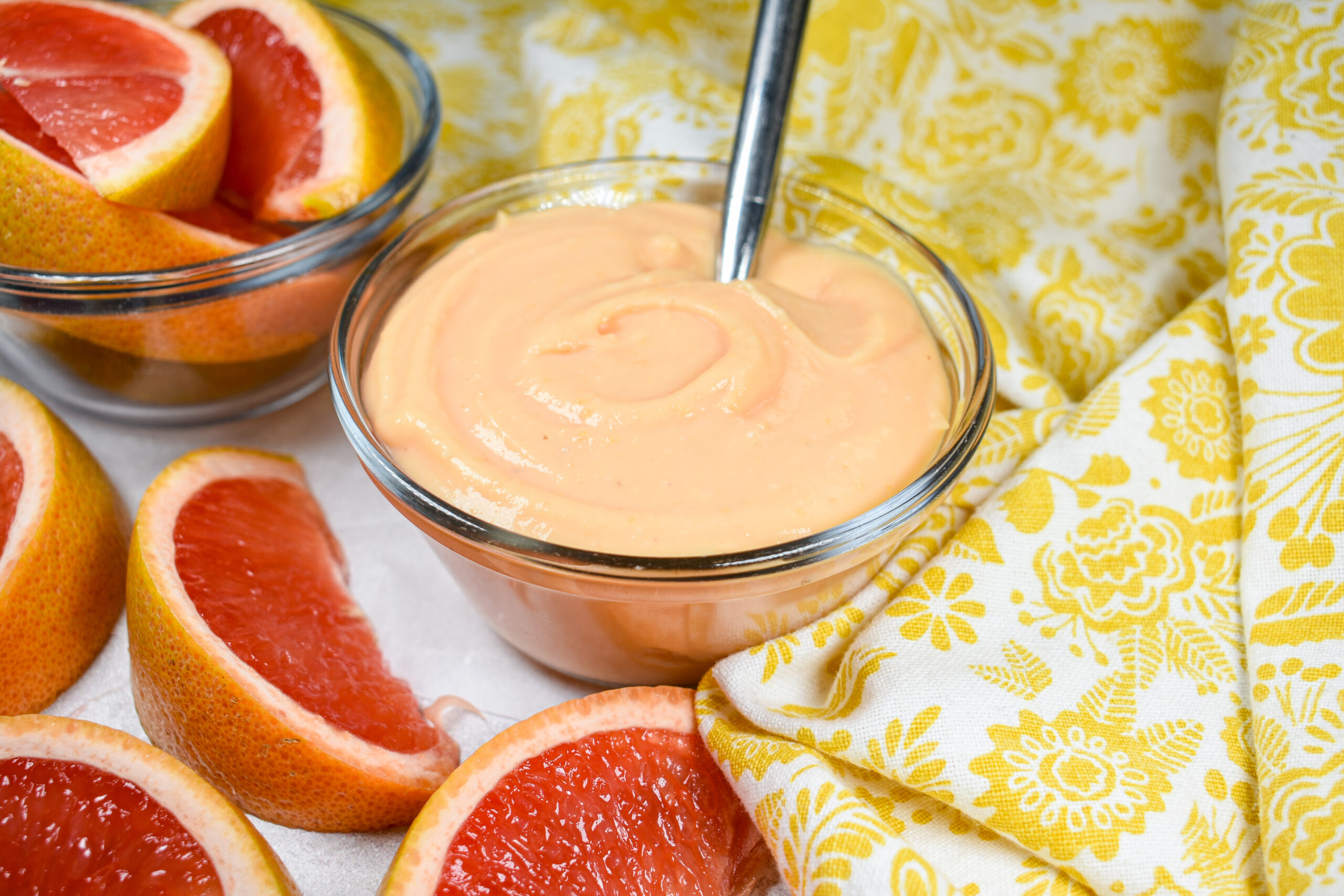 A dish of grapefruit curd, yellow tea towel, and wedges of fresh citrus