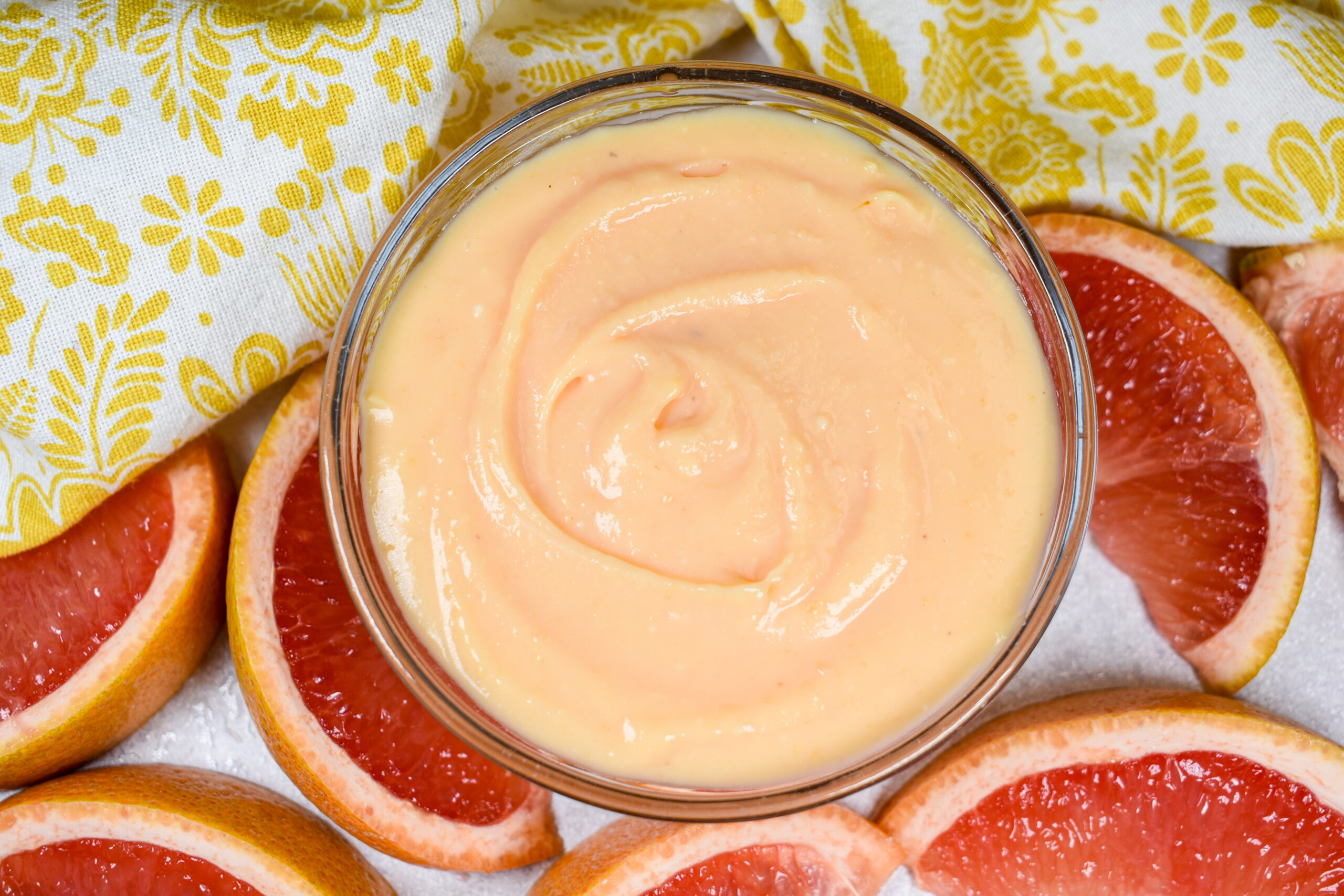 A dish of grapefruit curd surrounded by wedges of fresh grapefruit