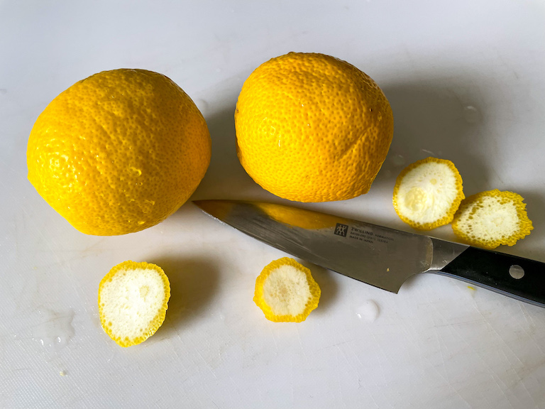 Two lemons with the ends sliced off, on a chopping board with a knife