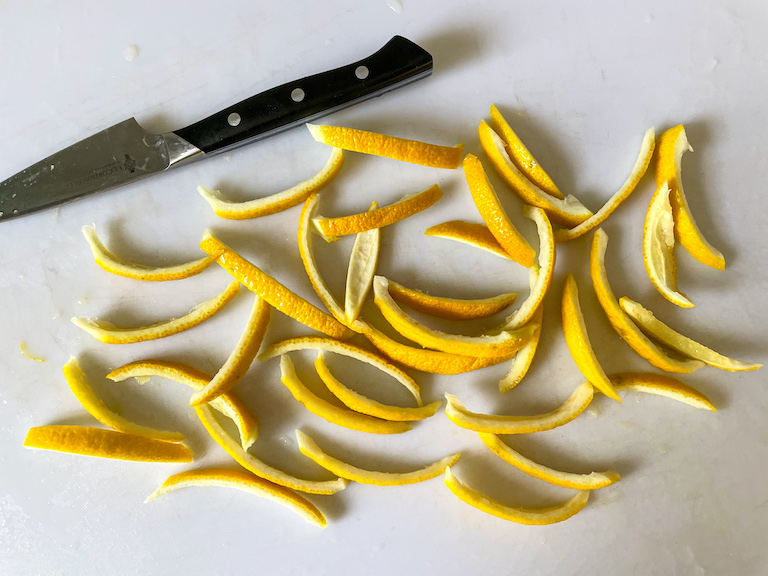 Lemon peel slices on a chopping board with a knife