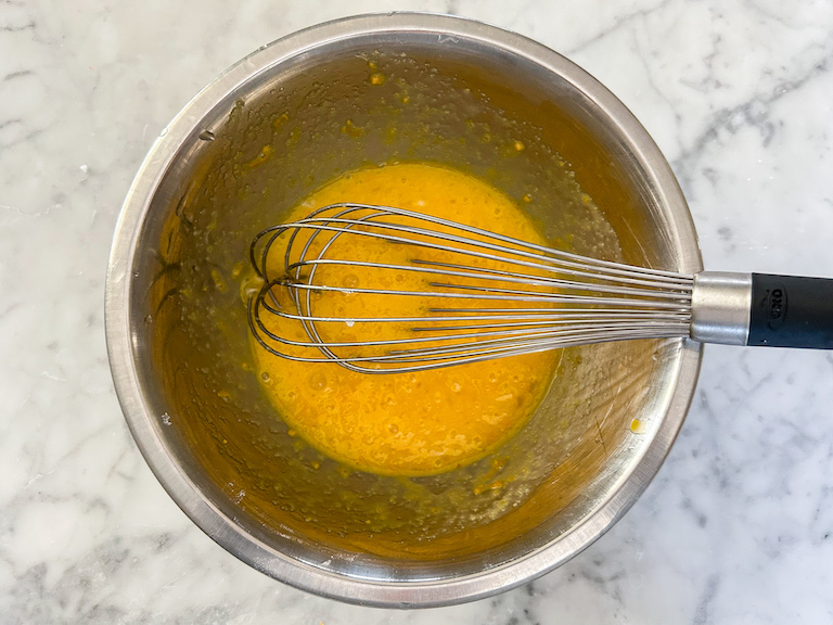 Wire whisk whisking curd ingredients in a bowl on a marble countertop