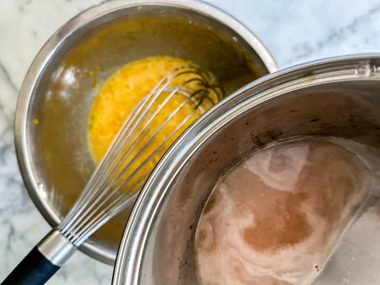 Saucepan pouring grapefruit juice into a bowl of whisked eggs
